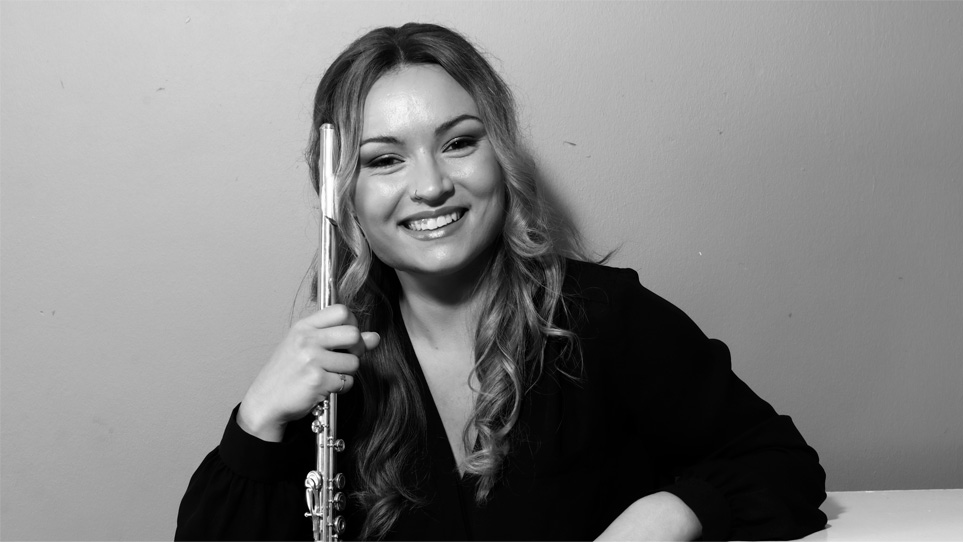 A women with mid-length hair, wearing a black shirt, holding her flute, smiling at the camera.